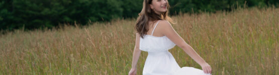 High school senior girl twirling in a white dress in a field at sunset in Newton, Massachusetts – senior portrait by Adriana Kopinja Photography.