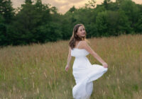 High school senior girl twirling in a white dress in a field at sunset in Newton, Massachusetts – senior portrait by Adriana Kopinja Photography.